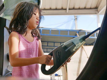 Little girl, 4 years old, cleaning a car using a portable handheld vacuum cleaner 