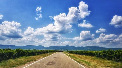 Empty road amidst field against sky