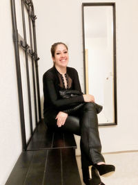 Portrait of a smiling young woman sitting against wall