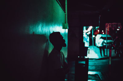 Rear view of man standing against illuminated wall