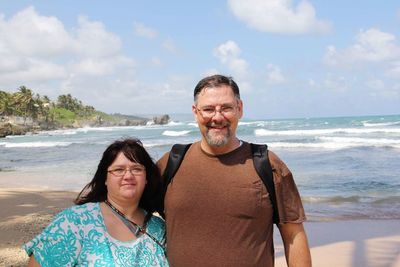 Portrait of smiling overweight couple standing at beach against sky