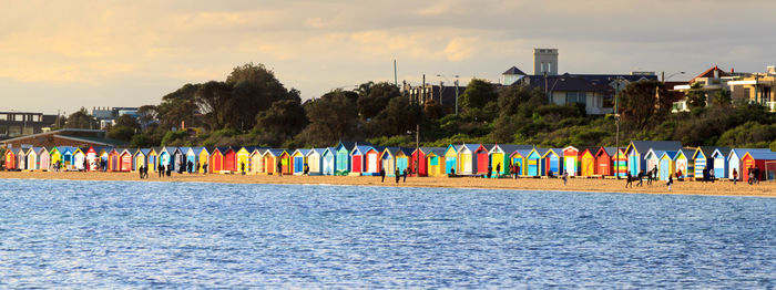 Scenic view of beach by colourful bathing boxes against sky