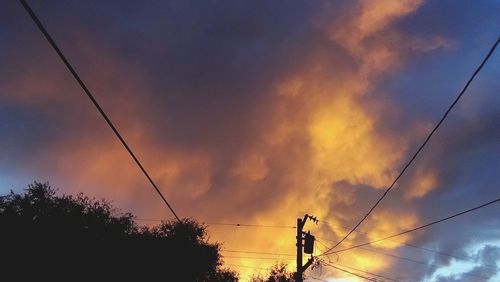 Low angle view of electricity pylon against cloudy sky