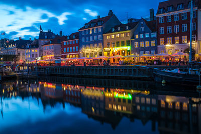 Illuminated buildings by river against sky in city at night