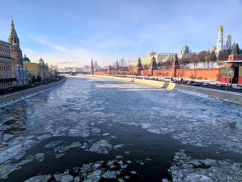 High angle view of frozen river by buildings against sky