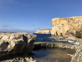 Rock formations by sea against blue sky