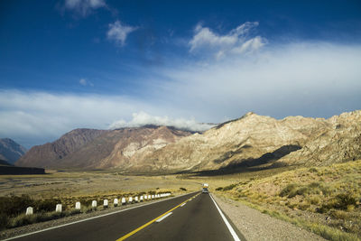 Road leading towards mountains against blue sky