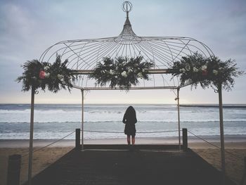 Rear view of woman standing at beach against sky