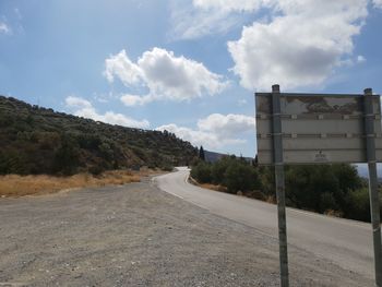 Empty road by trees against sky in city