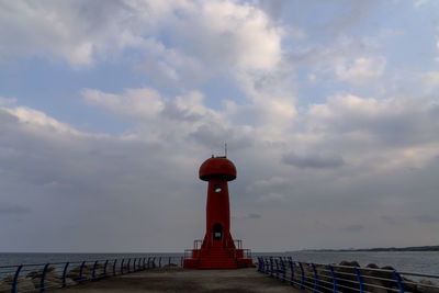 Lighthouse on pier by sea against sky
