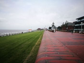 Footpath by sea and buildings against sky