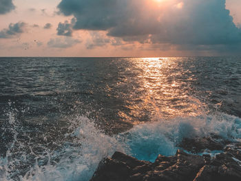 Splashing water of sea against sky during sunset