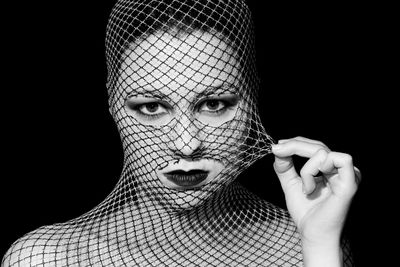 Close-up portrait of woman wearing lipstick and netting against black background