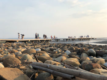 Group of people on rocks at beach against sky