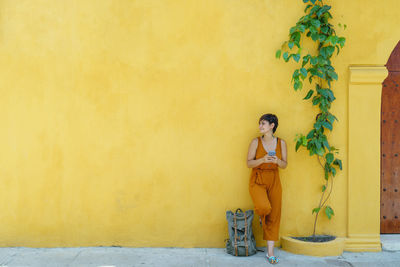 Young woman standing against yellow wall