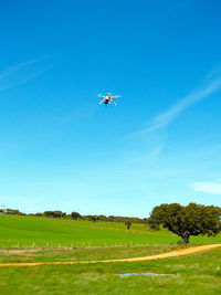 Airplane flying over field against clear blue sky