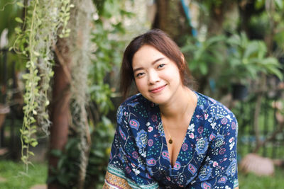 Portrait of young woman standing against tree
