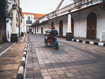 Rear view of man riding motorcycle on street amidst buildings in city