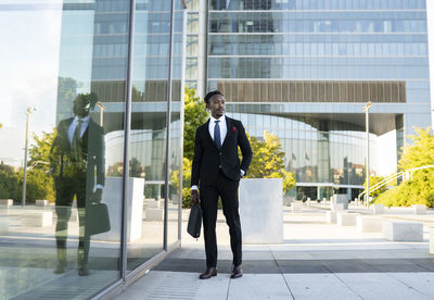 Serious african american male entrepreneur wearing elegant suit walking along glass office building in city center and looking away