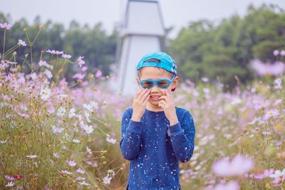 Boy wearing sunglasses standing amidst flowering plants on field