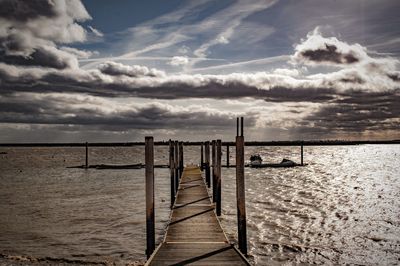 Wooden posts in sea against sky