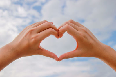 Close-up of woman hand holding heart shape against sky