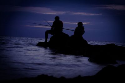 Silhouette men on sea against sky at night