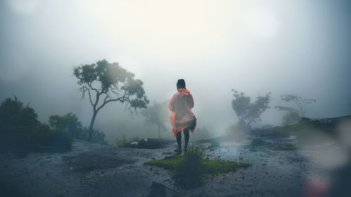 Rear view of man wearing raincoat while standing amidst fog during rainy season