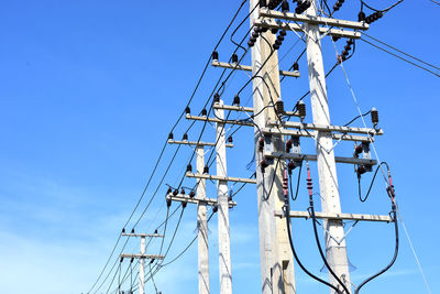 Low angle view of electricity pylon against blue sky