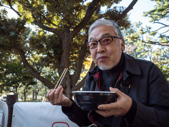 An older asian man eating noodles and soup with chopsticks