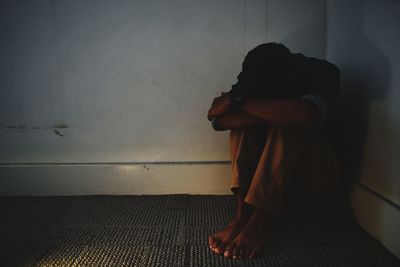 Side view of a woman sitting against wall