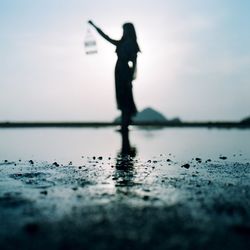 Surface level of silhouette woman standing at lakeshore against sky