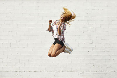 Happy young woman jumping mid-air in front of white wall