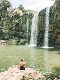 Rear view of woman sitting by waterfall