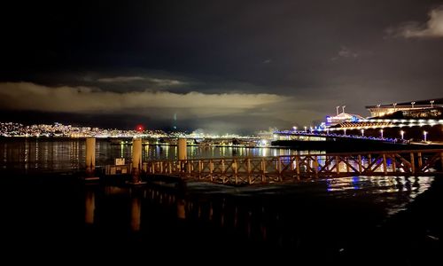 Illuminated bridge over river against sky in city at night