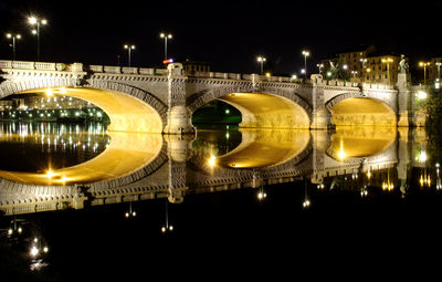 Illuminated arch bridge over po river against sky in city at night