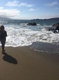 Rear view of man standing on beach against sky