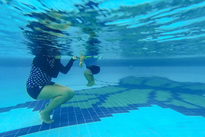 Low section of mother and baby boy swimming in pool underwater