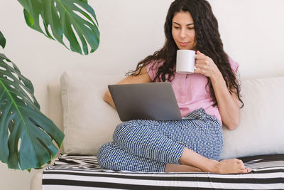 Young woman using phone while sitting on laptop