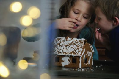 Siblings eating gingerbread house on table