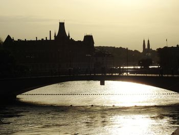 Silhouette of buildings by river during sunset