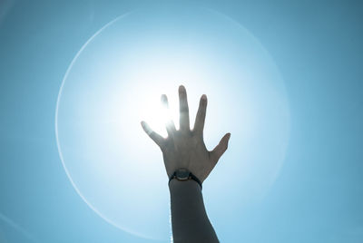 Cropped image of person reaching towards bright sun