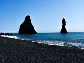 Rocks on beach against clear blue sky