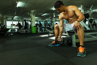 Shirtless muscular man lifting dumbbell while exercising at gym