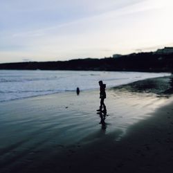 Silhouette girl standing on beach against sky during sunset