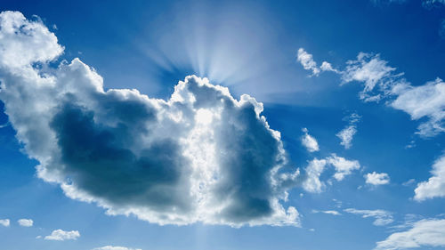 Low angle view of sunlight streaming through clouds