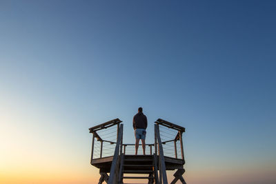 Rear view of man sitting against clear sky