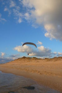 Mid distance view person paragliding over beach against sky