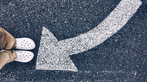 Low section of person standing by arrow symbol on road