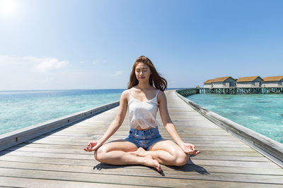 Woman doing yoga amidst sea on pier during sunny day